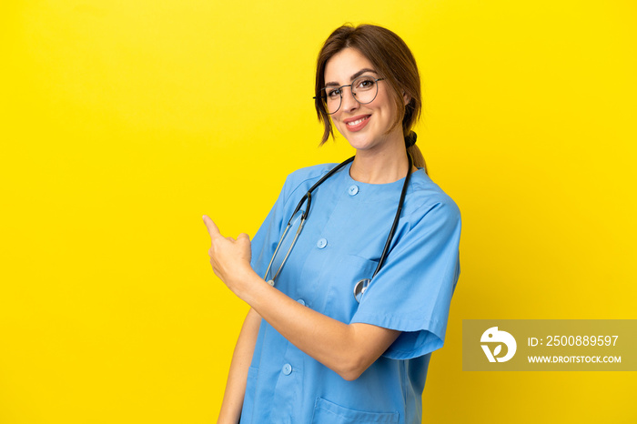 Surgeon doctor woman isolated on yellow background pointing back