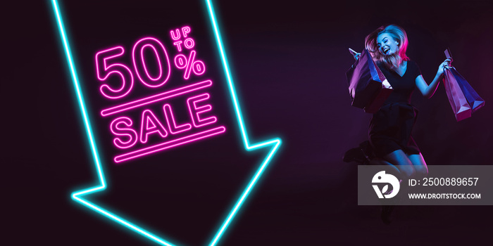 Cheerful, jumping. Portrait of young woman in neon on dark studio backgound. Human emotions, black friday, cyber monday, purchases, sales, finance concept. Copyspace. Seamless post for instagram.