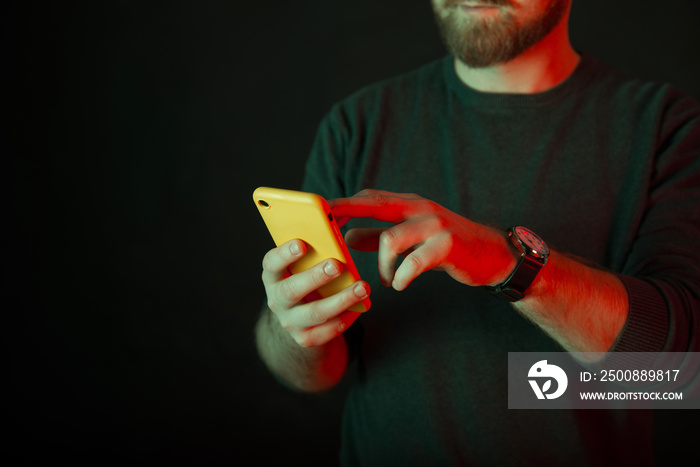 Crop photo of a faceless bearded man using a yellow phone over dark black background shot in a studio.