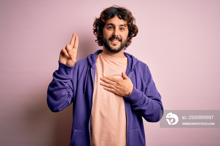 Young handsome sporty man with beard wearing casual sweatshirt over pink background smiling swearing with hand on chest and fingers up, making a loyalty promise oath