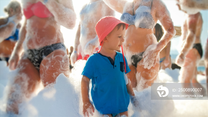 Image of happy 3 years old toddler boy with young mother having fun and dancing on the beach soap foam disco party, Family relaxing on summer holiday vacation.