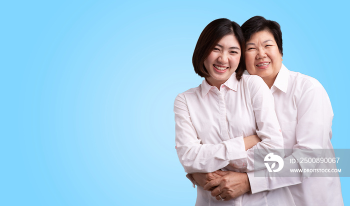 Beautiful senior mom and her adult daughter are hugging, looking at camera and smiling