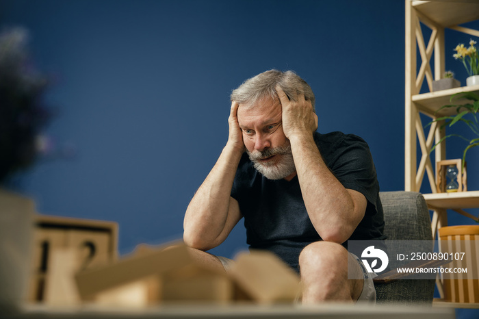 Loosing all the memories. Old bearded man with alzheimer desease sitting on the chair and suffering from headache. Concept of illness, memory loss due to dementia, healthcare, depression, stress out.