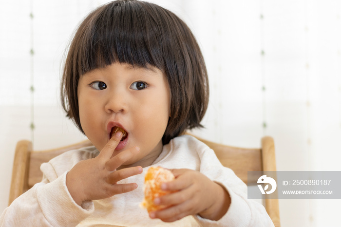 座ってミカンを食べる赤ちゃん（2歳4か月、女の子、日本人）