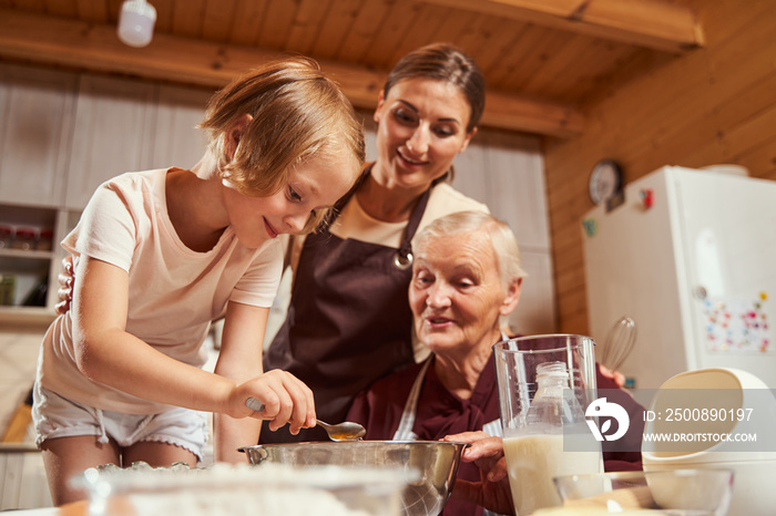 Child holding teaspoon above deep plate with her family watching