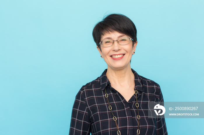 Fashion, people and style concept - Beautiful mid-aged woman wearing eye-glasses laughing on blue background with copy space