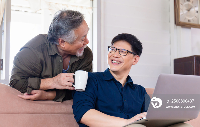 Cheerful old senior mature father and adult son talking conversation at home, Happy asian father and middle aged son using computer laptop in living room