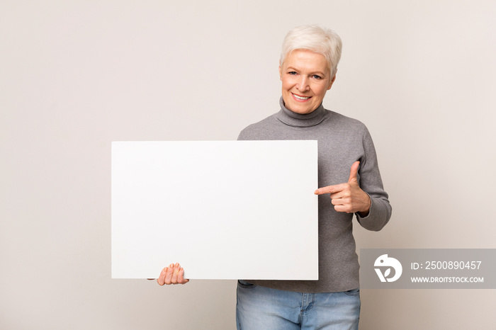 Senior woman holding blank advertising board and pointing on it