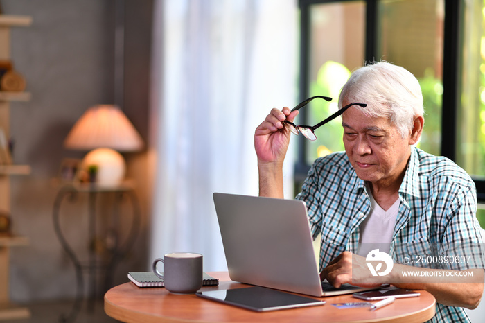 Asian senior man using laptop in living room at home