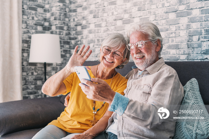 Happy retired family couple using mobile phone for video call together, talking to relations, getting good news, having fun, smiling and laughing. Carefree mature pensioners chatting online on cell.