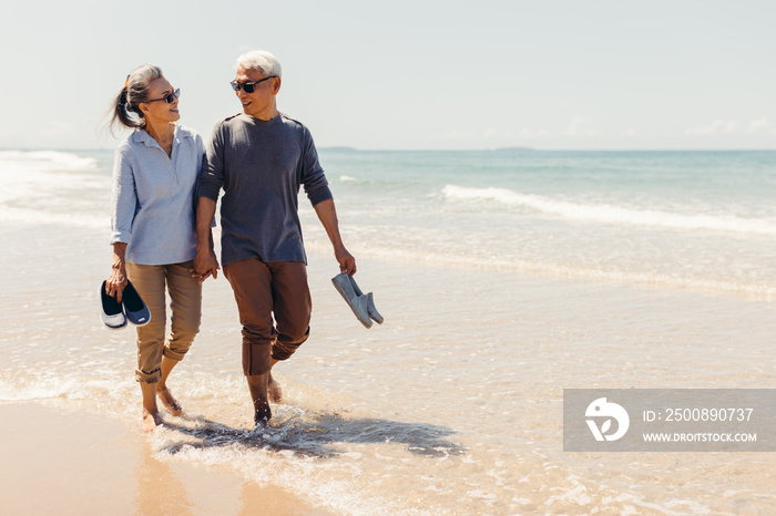 Romantic Senior couple strolling happily along the beach in the sunshine and bright sky. Retirement concept and happy life.