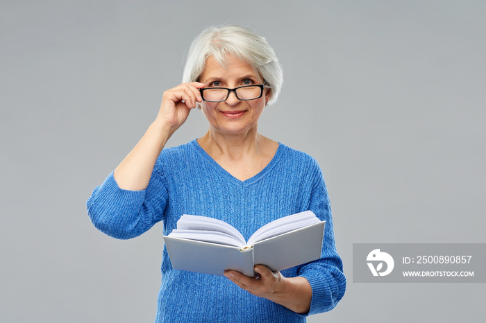 vision, wisdom and old people concept - smiling senior woman in glasses reading book over grey background