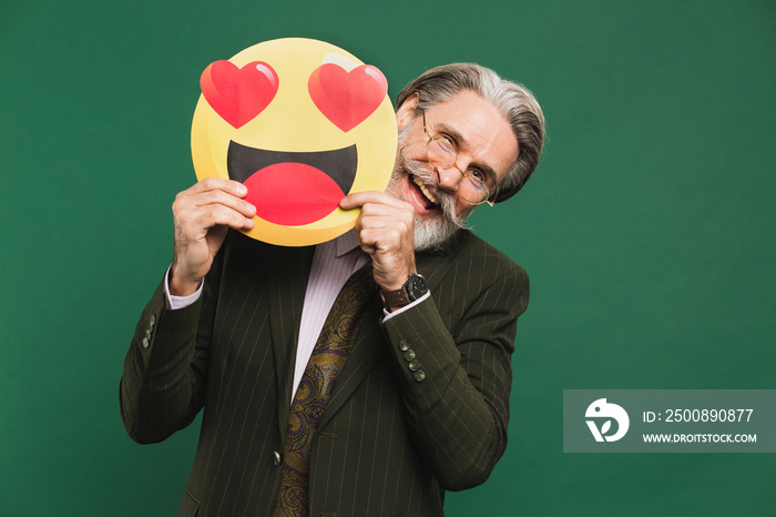 Business middle-aged bearded man in khaki suit holding emoji with hearts in eyes on a green background