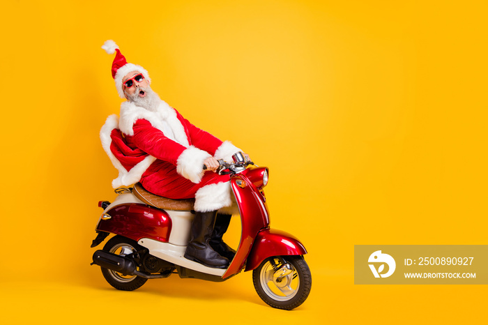 Full body photo of santa grandpa riding x-mas party by bike shocking moped speed wear stylish sun specs red coat trousers cap shirt boots isolated yellow color background