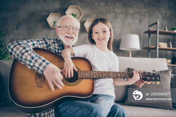 Photo of funny aged old grandpa little pretty granddaughter holding playing guitar teaching bonding duet spend time together stay home quarantine safety modern interior living room indoors