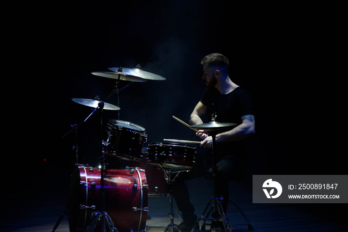 music, people, musical instruments and entertainment concept - male musician with drumsticks playing drums on the stage.