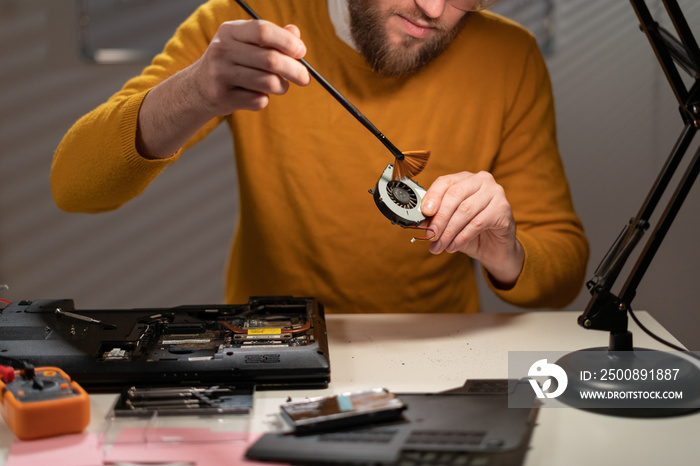 Disassembling and fixing a laptop computer and cleaning its cooling system with little brush. Dust and dirt on computer fan