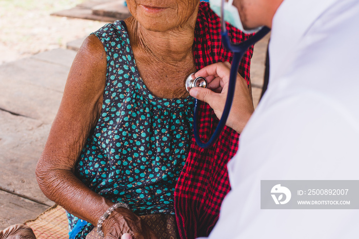 Male Doctor listening heart beat and breathing of Elderly Woman with Stethoscope with First Aid Medical Box.Community Health and Development Hospital In Remote Areas Development Fund Concept.