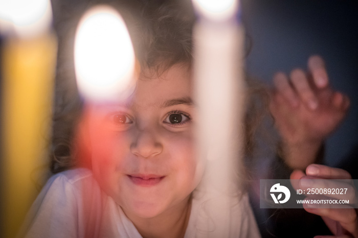 Isolated close up portrait of a beautiful five year old girl looking at Hanukkah candles