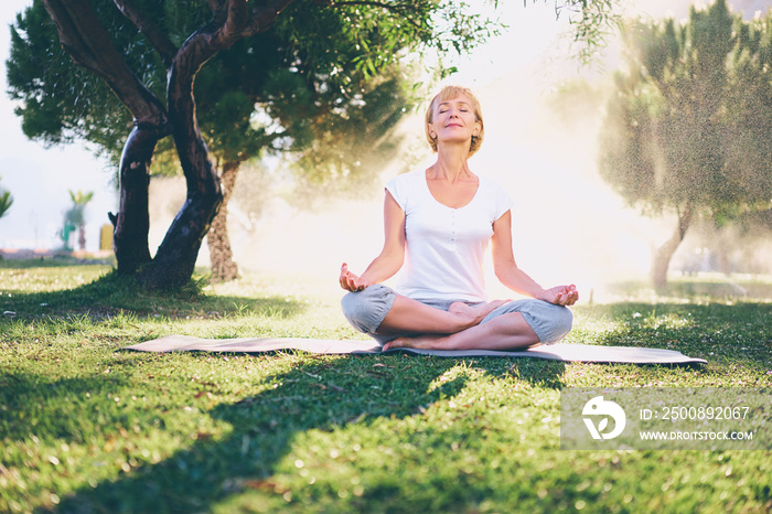 Yoga at park. Senior woman in lotus pose sitting on green grass. Concept of calm and meditation.