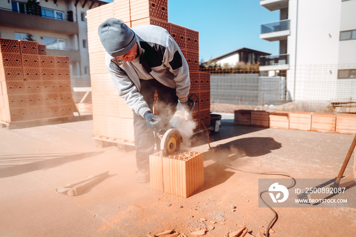 worker using an angle grinder on construction site for cutting bricks, debris. Tools and bricks on new building site