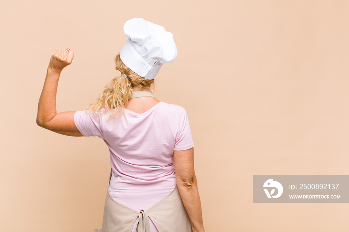 middle age woman baker standing and pointing to object on copy space, rear view