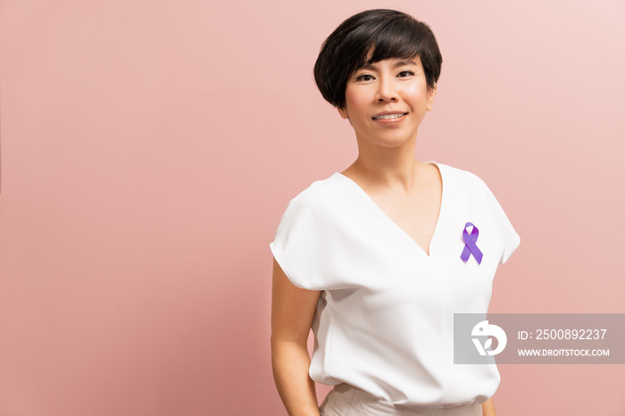 Portrait of beautiful and stylish Asian middle aged woman stand, wear white blouse top with purple ribbon pin on pastel pink tone background. Support stop domestic violence awareness month campaign.