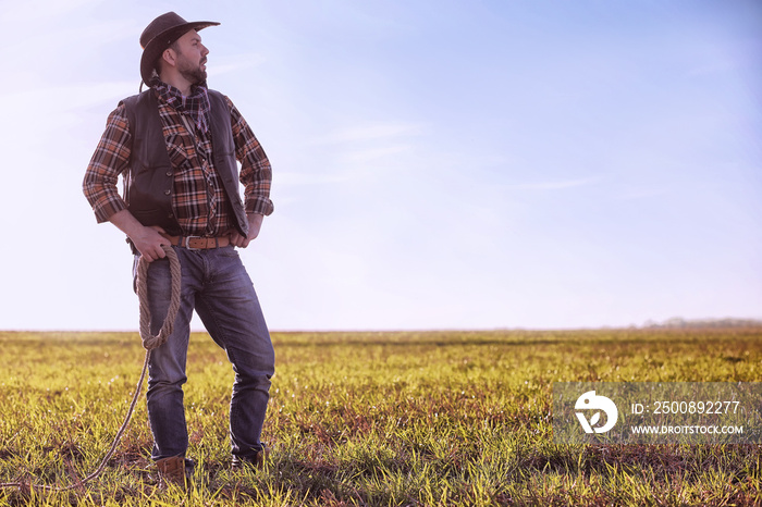 Cowboy standing in a field at sunset