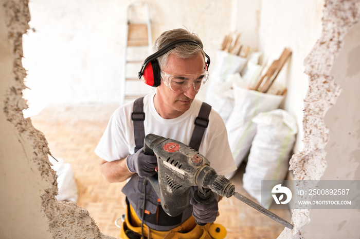 Senior worker using drill at contruction site