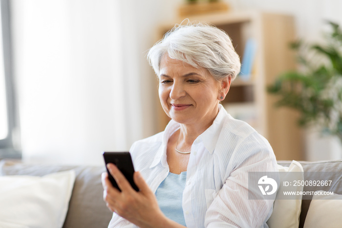 technology, communication and people concept - happy senior woman with smartphone at home