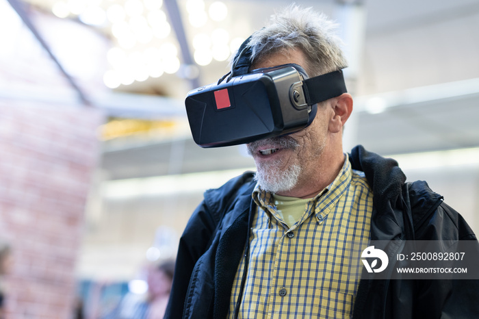 Casual senior bearded man wearing virtual reality goggles watching virtual presentation of a business idea concept at business fair of modern artificial intelegence technology.