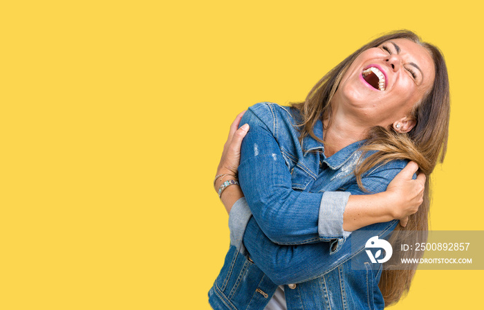 Beautiful middle age woman wearing casual denim jacket over isolated background Hugging oneself happy and positive, smiling confident. Self love and self care