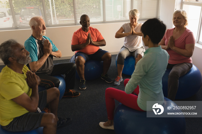 Female trainer training senior people in performing yoga