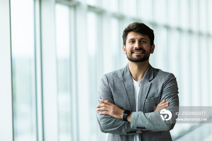 Confident businessman standing with arms folded at modern office