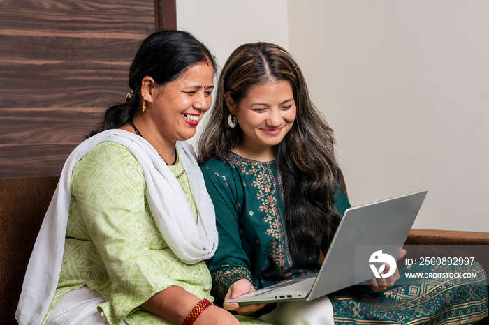 Indian mother and daughter watching into the laptop at home. Modern daughter helping her mother with technology. Mother and daughter at home.