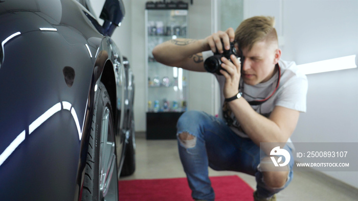 A young professional photographer (a guy, a man) takes pictures of a car in a car salon. Concept: lifestyle, new photo, car, photo apron, flash, exhibition.