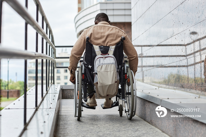 Back view of man with disability pushing wheelchair wheel while going down ramp in city, copy space