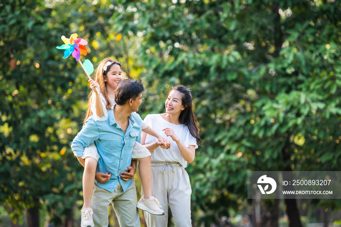 Happy asian playing colorful windmill toy enjoy funny family time in park with sunlight sky background.