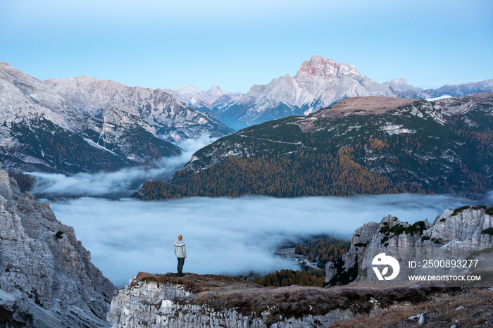 A tourist stands over the fog at the edge of a cliff in the Dolomites mountains. Location Auronzo rifugio in Tre Cime di Lavaredo National Park, Dolomites, Trentino Alto Adige, Italy