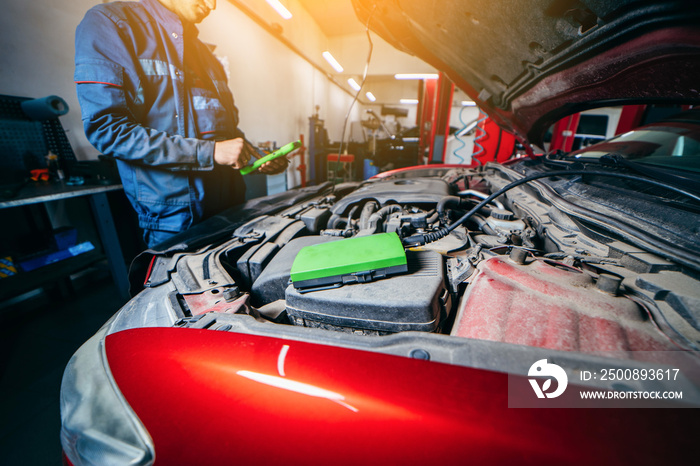 Car service electrician or mechanic uses a tablet computer with futuristic interactive diagnostics software. Inspecting the vehicle in order to find broken components in the engine bay of modern car