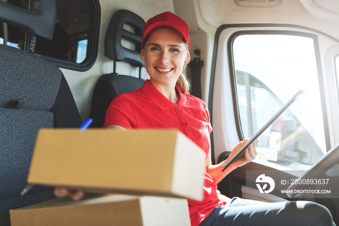 young happy female delivery service worker sitting in van and delivering a box