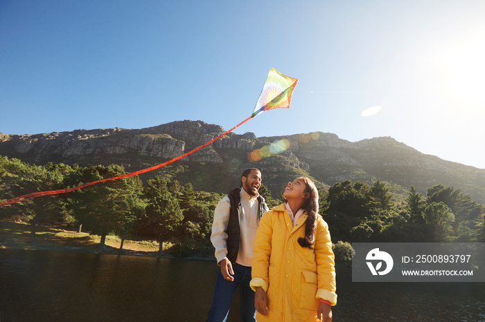 Father and daughter watching kite flying during family camping trip with mountain backdrop and blue sky