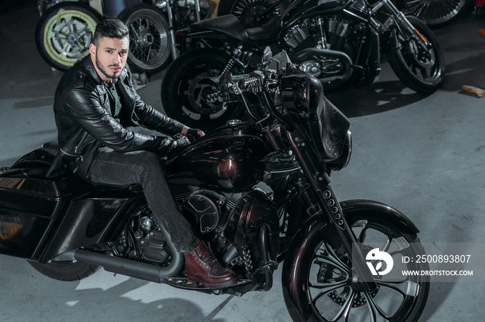 high angle view of handsome young man in leather jacket sitting on bike at garage