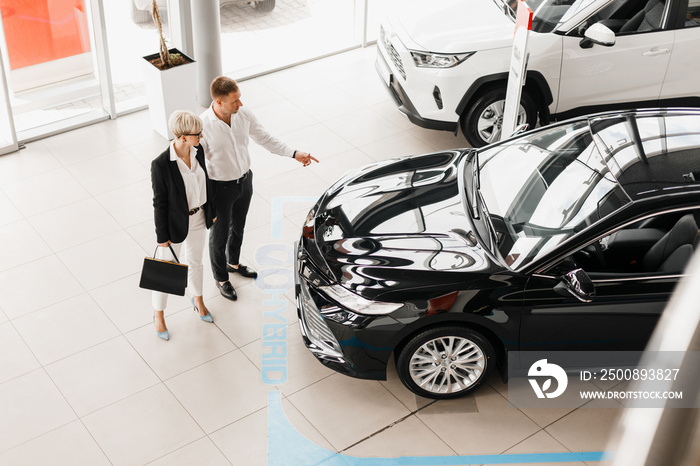 Family couple in dealership choose a car, man pointing to automobile. Top view