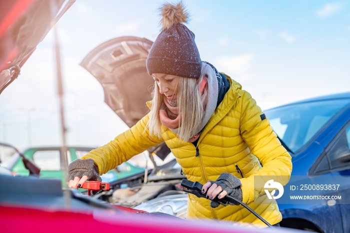 Beauty woman with her car broken down. Girl trying to start her broken car with discharged flat battery