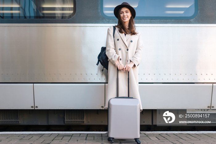 Beautiful woman tourist with  suitcase on the background of  passenger train car at the railway station