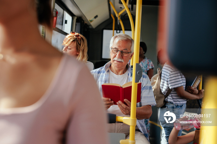 Senior man reading book in bus