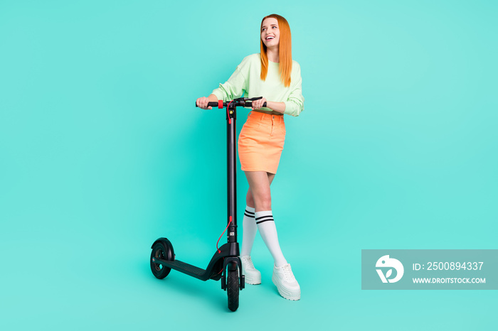 Full length photo of charming happy dreamy woman look empty space hold scooter isolated on teal color background