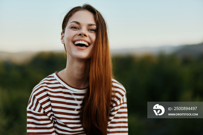 Young woman in a striped t-shirt smiles cutely on a journey against the backdrop of autumn nature