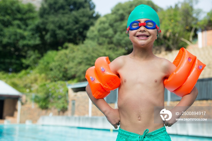 Boy wearing arm bands standing at poolside